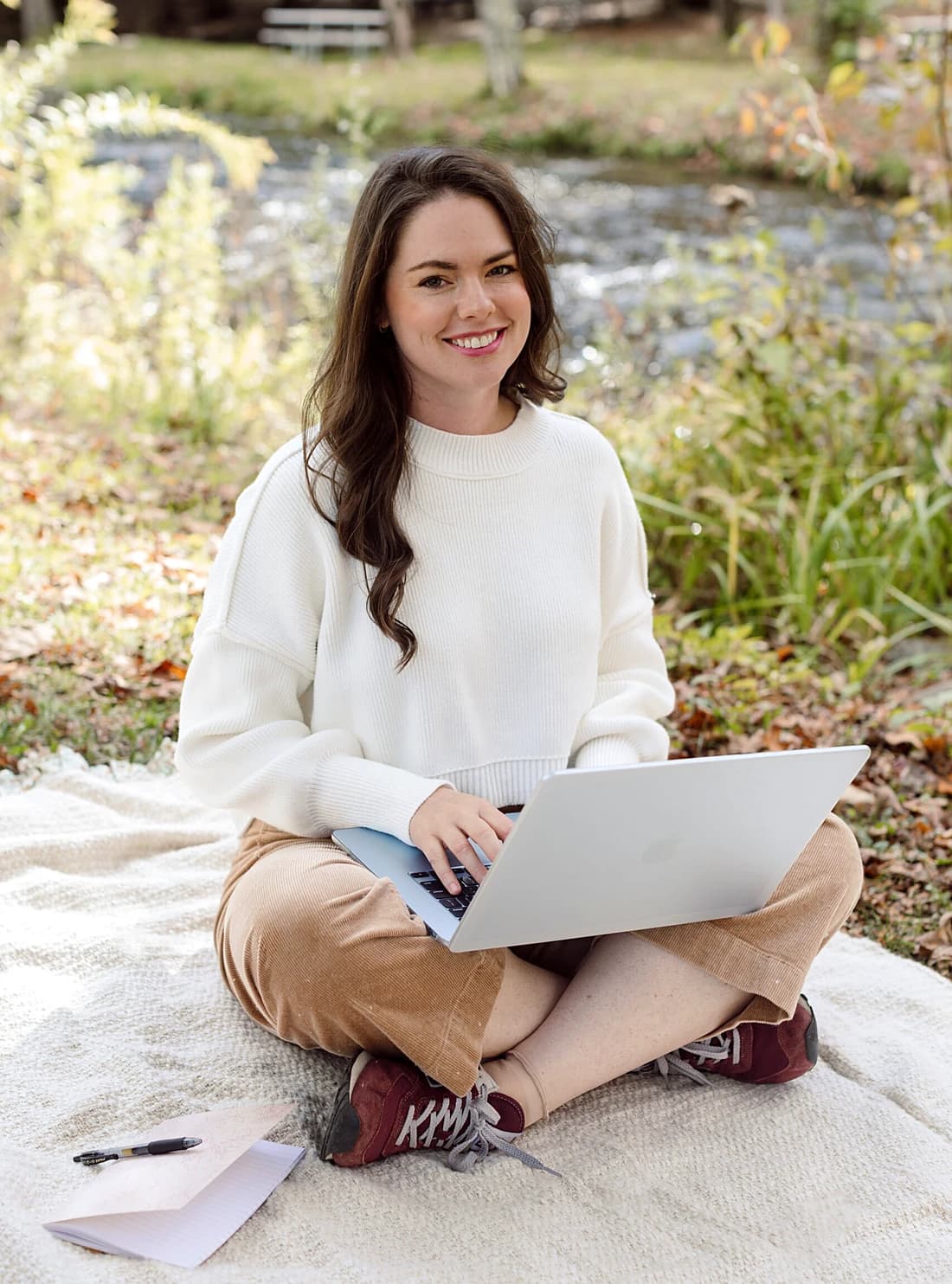 Emily sitting cross-legged on a blanket outdoors, working on a laptop